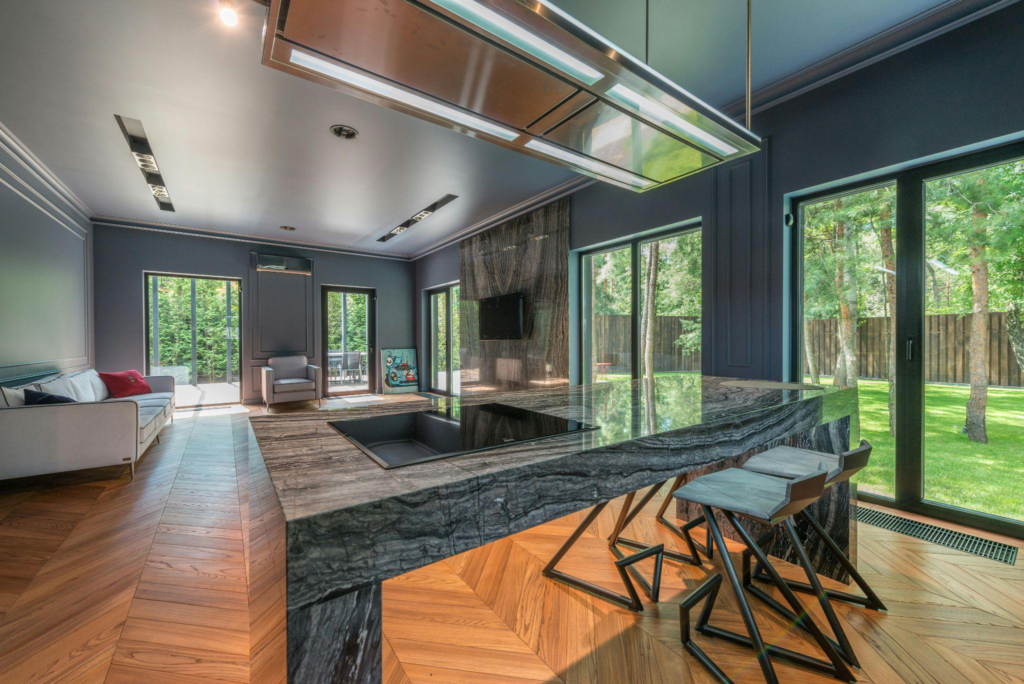 Modern kitchen and living area with large floor-to-ceiling windows and outdoor view.
